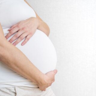 امرأة حامل ترتدي كنزة بيضاء وتضع يديها على بطنها