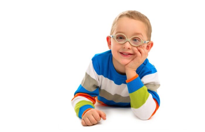 صبي مصاب بالحول يرتدي نظارات وكنزة مخططة بالأزرق والأبيض يجلس مبتسما على الأرض