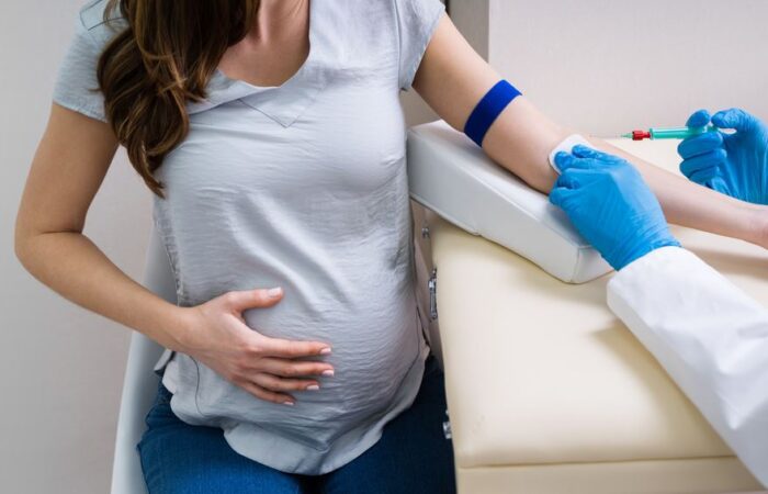 طبيب يلبس قفازات زرقاء ويقوم بتوجيه إبرة نحو يد امرأة حامل تجلس أمامه