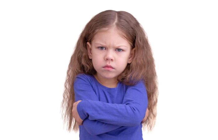 فتاة صغيرة ترتدي كنزة زرقاء وتقف بعصبية مكتوفة اليدين