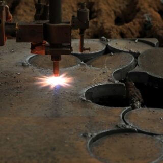 ماكينة لها رأس اسطواني يخرج منه لهب موجه يقوم بقطع صفيحة معدنية سميكة أسفله الى قطع دائرية صغيرة