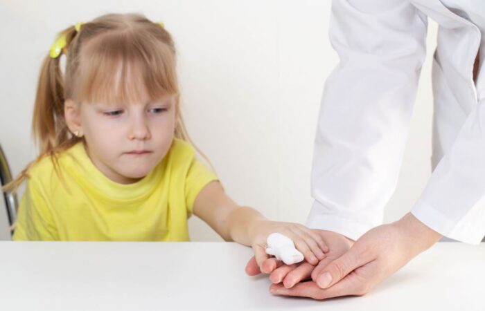 فتاة صغيرة ترتدي كنزة صفراء وفي إصبعها جهاز قياس و تقوم بوضع يدها على يد شخص يرتدي كنزة بيضاء جانبها