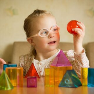 فتاة من ذوي الاحتياجات الخاصة ترتدي نظارات زهرية وتلعب بألعاب موجودة أمامها على الطاولة