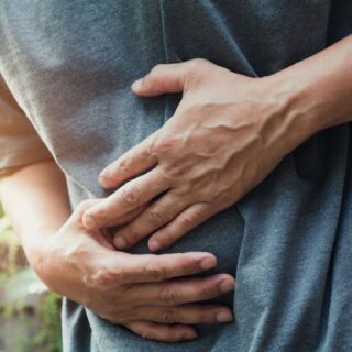 شخص بالغ يرتدي كنزة رمادية ينحني للأمام ويضع يديه على بطنه