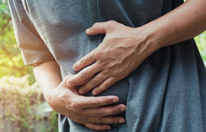 شخص بالغ يرتدي كنزة رمادية ينحني للأمام ويضع يديه على بطنه