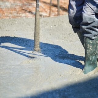 عامل بناء يمسك بجهاز اسطواني يهتز ويقوم بسحبه من مادة طينية رمادية اللون