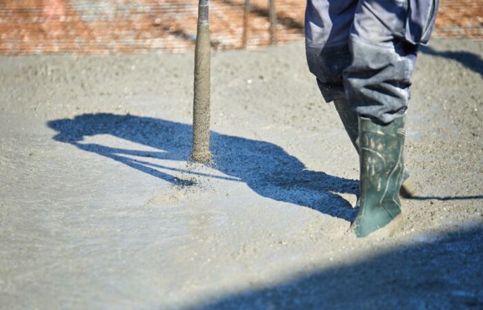 عامل بناء يمسك بجهاز اسطواني يهتز ويقوم بسحبه من مادة طينية رمادية اللون