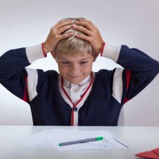 صبي يجلس أمام طاولة الدراسة ويضع يديه على رأسه