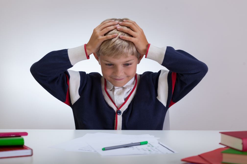 صبي يجلس أمام طاولة الدراسة ويضع يديه على رأسه