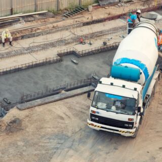 شاحنة لها هيكل اسطواني كبير يستخدم لنقل المواد الاسمنتية تقوم بإفراغ حمولتها في موقع للبناء