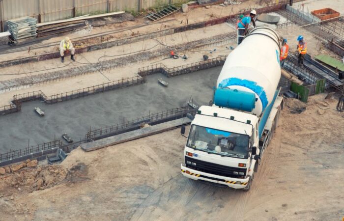 شاحنة لها هيكل اسطواني كبير يستخدم لنقل المواد الاسمنتية تقوم بإفراغ حمولتها في موقع للبناء