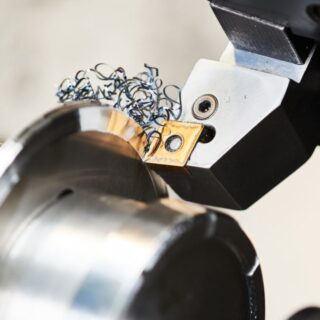 ماكينة هندسية لها رأس ذهبي حاد يقوم بقطع قطعة معدنية اسطوالنية الشكل أمامه