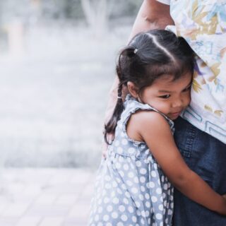 فتاة صغيرة تشعر بالخجل وتقوم بحضن قدم رجل يقف بجانبها ويقوم هو بوضع يده على ظهرها