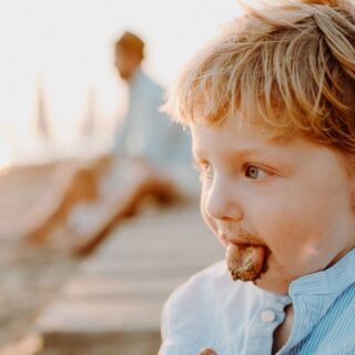 ولد صغير على شاطئ البحر يمد لسانه للخارج ويظهر على اللسان رمل البحر