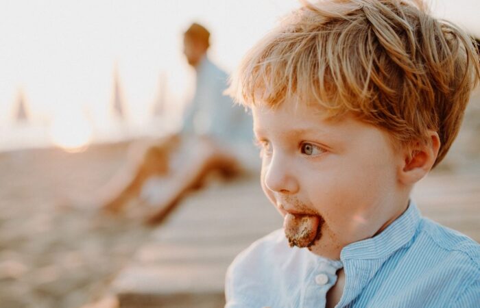 ولد صغير على شاطئ البحر يمد لسانه للخارج ويظهر على اللسان رمل البحر