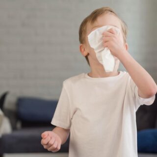 ولد صغير يرتدي كنزة رمادية يضع قطعة من المحارم على وجهه