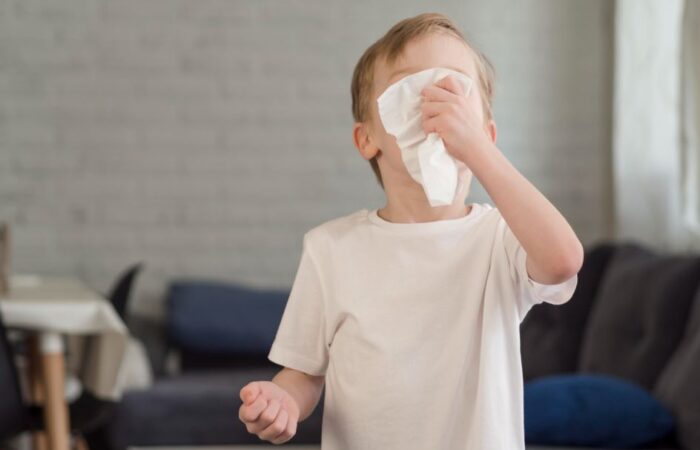 ولد صغير يرتدي كنزة رمادية يضع قطعة من المحارم على وجهه