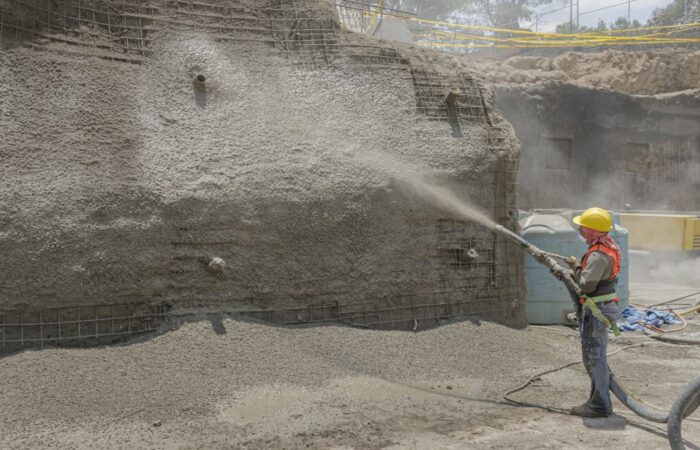 عامل بناء يرش الخرسانة على جدار فيه شبكة من القضبان المعدنية في موقع البناء