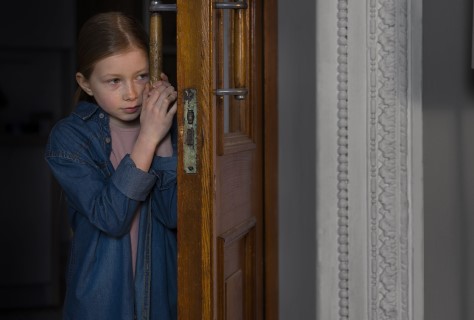 فتاة ترتدي قميص أزرق تقف خلف الباب وهي خائفة