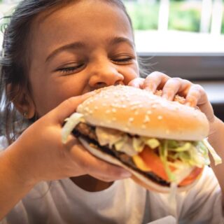 فتاة صغيرة تتناول قطعة من الهمبرغر بشراهة