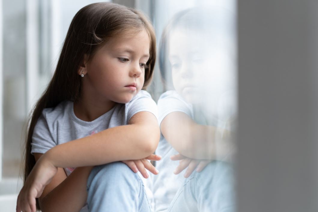 فتاة صغيرة مصابة بصدمة عاطفية تجلس جانب النافذة
