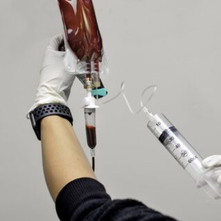 شخص يحمل ابرة طبية كبيرة الحجم ويقوم بضخ غاز داخل كيس شفاف يحتوي على سائل أحمر اللون