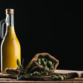 زجاجة تحتوي على سائل أصفر اللون وبجانبها مجموعة من حبوب الزيتون الأخضر داخل كيس صغير بني