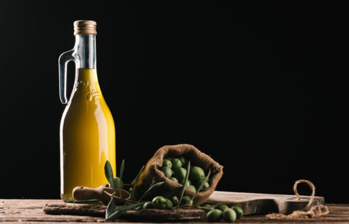 زجاجة تحتوي على سائل أصفر اللون وبجانبها مجموعة من حبوب الزيتون الأخضر داخل كيس صغير بني