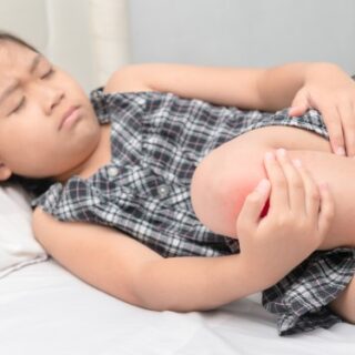 فتاة تجلس على السرير وتمسك ركبتها بيدها