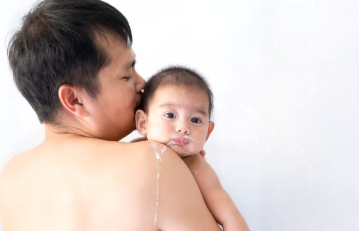 رجل بالغ يحمل طفل رضيع حيث يظهر على كتف الرجل سائل أبيض اللون