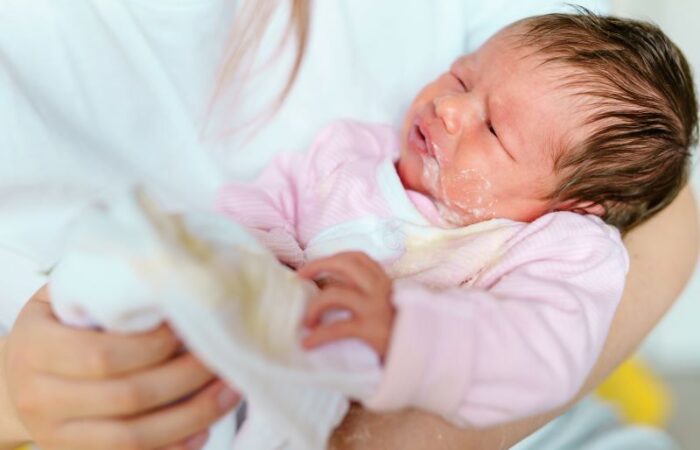 امرأة تحمل طفلة رضيعة بين يديها وهي تتقيأ الحليب