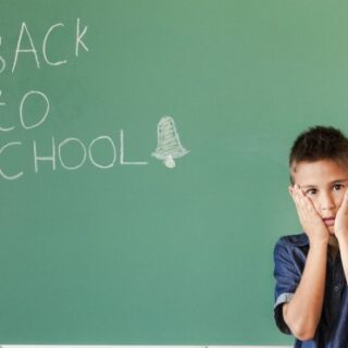 طفل خائف يقف جانب لوح مدرسي مكتوب عليه بالانكليزي عبارة العودة للمدرسة