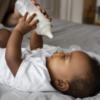 طفل رضيع أسمر اللون يمسك زجاجة الحليب بيديه