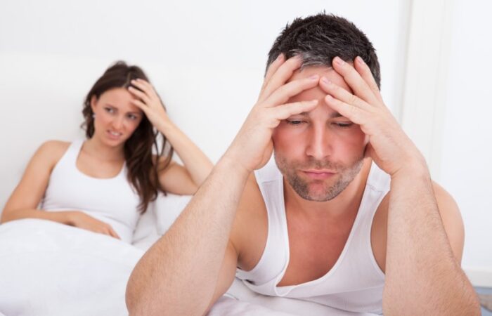 رجل يضع يديه على رأسه ويجلس على السرير وبجانبه إمراه