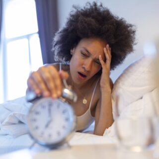 فتاة تضع يدها على رأسها واليد الأخرى تضعها على ساعة منبه لها أجراس