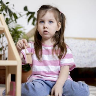 فتاة ترتدي كنزة مخططة باللونين الزهري والأبيض تلعب وهي جالسة على الأرض وتقوم بمراقبة شخص ما