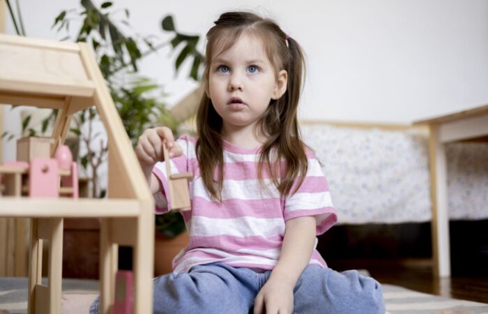 فتاة ترتدي كنزة مخططة باللونين الزهري والأبيض تلعب وهي جالسة على الأرض وتقوم بمراقبة شخص ما