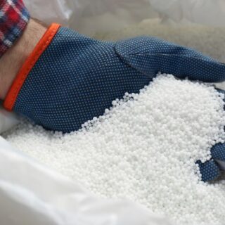 حبيبات كروية بيضاء داخل كيس أبيض ويقوم شخص يلبس كفّ أزرق بفحصها