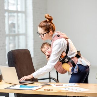 امرأة تعمل بمكتبها وتحمل طفلها بين ذراعيها