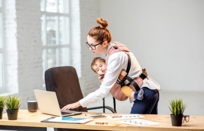 امرأة تعمل بمكتبها وتحمل طفلها بين ذراعيها