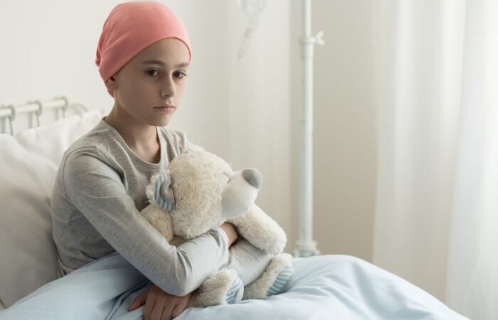 فتاة حزينة تجلس على السرير محتضنة لعبة الدب وتضع قبعة حمراء على رأسها