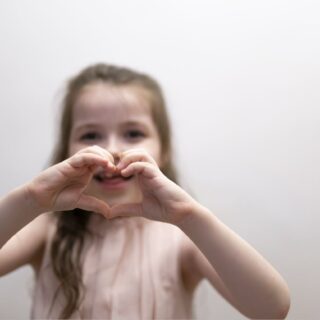 فتاة صغيرة تقوم بتشكيل قلب الحب بيديها وهي تبتسم