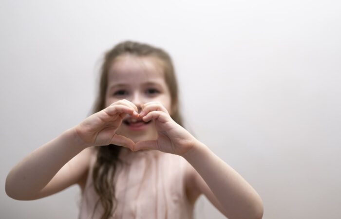 فتاة صغيرة تقوم بتشكيل قلب الحب بيديها وهي تبتسم