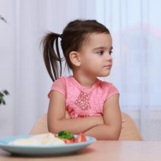 فتاة تجلس على الكرسي وترفض تناول الطعام الموجود أمامها على الطاولة