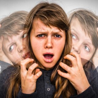 امرأة عاقدة الحاجبين ترفع يديها بشكل عصبي نحو الأمام وعلى جانبيها صورة مستنسخة لها