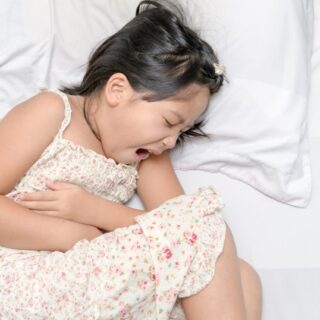 فتاة صغيرة مستلقية على السرير تصرخ مغمضة العينين وهي تضغط بيديها على بطنها