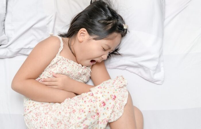 فتاة صغيرة مستلقية على السرير تصرخ مغمضة العينين وهي تضغط بيديها على بطنها