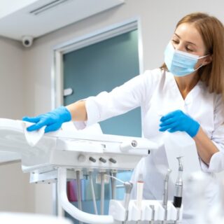 امرأة ترتدي لباس أبيض وقفازات زرقاء وتضع كمامة على وجهها وتقوم بمسح أدوات فحص الأسنان