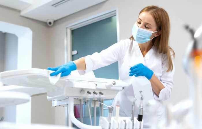 امرأة ترتدي لباس أبيض وقفازات زرقاء وتضع كمامة على وجهها وتقوم بمسح أدوات فحص الأسنان