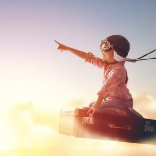 ولد يجلس عل حقيبة سفر تطفو فوق الغيوم ويشير بإصبع يده اليمنى للأمام